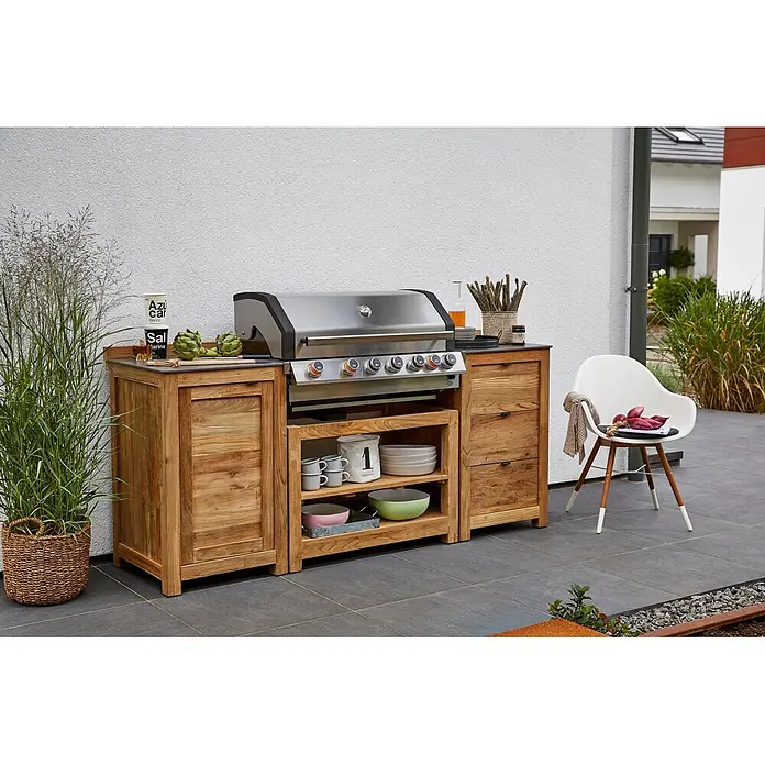 Sunfun Zoe Módulo de cocina exterior Armario con cajones - Marrón, An x Pr x Al: 58 x 63 x 92 cm, Madera de teca - Imagen de una parrilla de cocina exterior de madera moderna con parrilla de acero inoxidable, vajilla y una planta en el jardín.