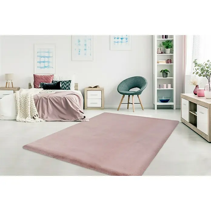 Fellteppich Happy - Rosa, 170 x 120 cm, 100 % Polyester (Flor) - Ein rosa Teppich liegt in einem hellen Schlafzimmer mit Bett, Stuhl und Regalen. Der Teppich ist der zentrale Fokus.