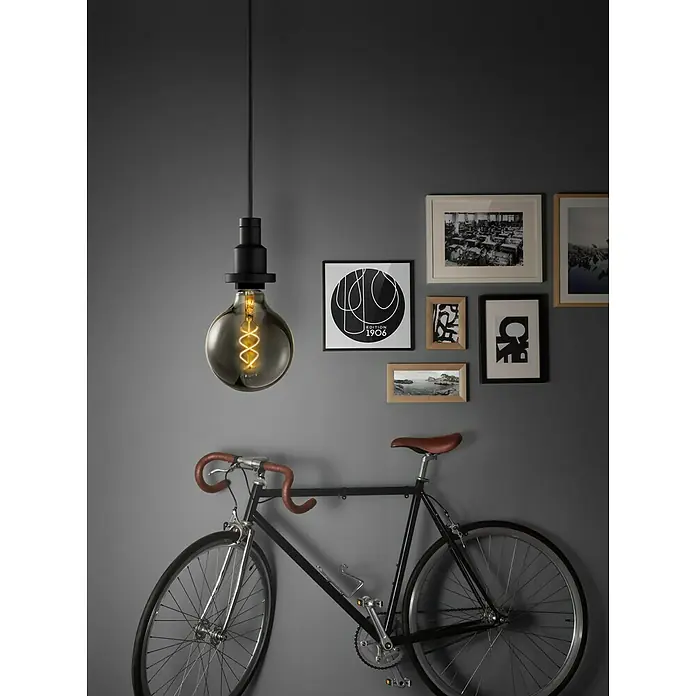 Osram Vintage 1906 Bombilla LED - E27, Blanco cálido, 150 lm, 5 W - Primer plano de una bombilla colgante con una bicicleta al fondo, creando un diseño de interior moderno y elegante.