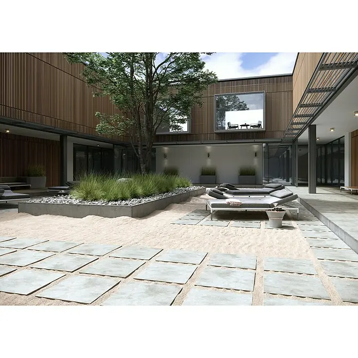 Cersanit Terrassenfliese Metropolis - 59,3 x 59,3 x 2 cm, Light Grey, Matt - Ein weitläufiger Innenhof mit Lounge-Bereich, Sandboden und Steinplatten lädt zum Verweilen ein. Die moderne Gestaltung wird durch üppige Vegetation ergänzt.