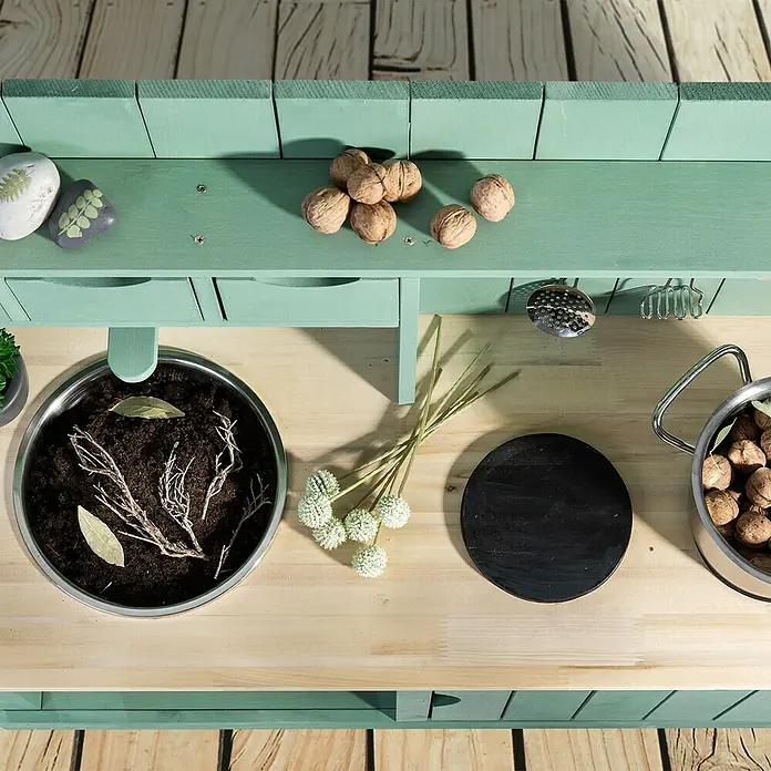 Muddy Buddy Matschküche Explorer - 102 x 40 x 105 cm, Holz, Salbeigrün - Detailansicht eines grünen Kinderspielküchen-Sets mit Utensilien wie Walnüssen, einem Topf und Pflanzen.