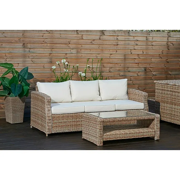 Mesa auxiliar de jardín Gotland - L x An x Al: 111 x 56 x 41 cm, Beige - Acogedor conjunto de muebles de jardín de ratán con sofá, mesa y macetero delante de una pared de madera, ideal para relajarse al aire libre.