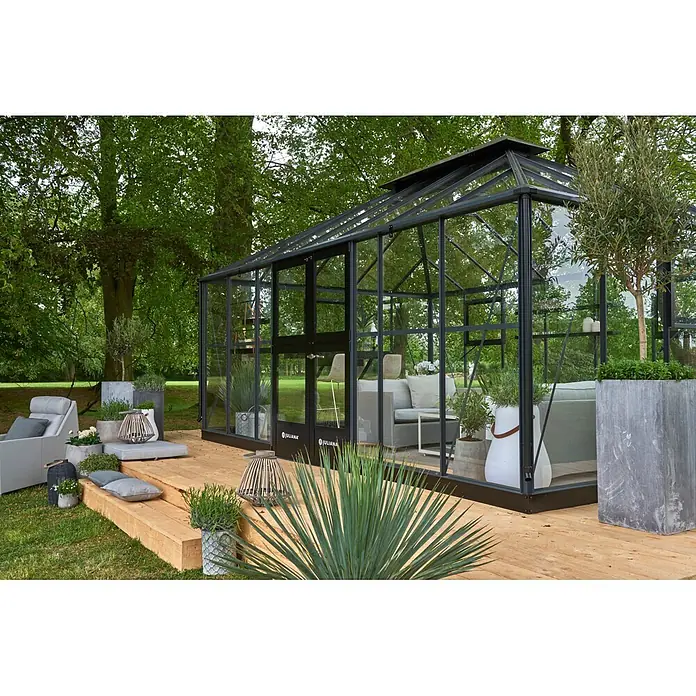 Juliana Gewächshaus Grand Oase - Außenmaß inkl. Dachüberstand (B x T): 368 x 511 cm, 3 mm, Anthrazit/Schwarz - Geräumiges Juliana Gewächshaus aus Glas und Metall mit Sitzbereich und Pflanzen auf einer Holzterrasse im Garten.