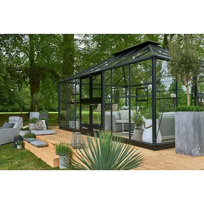 Juliana Gewächshaus Grand Oase - Außenmaß inkl. Dachüberstand (B x T): 368 x 511 cm, 3 mm, Anthrazit/Schwarz - Geräumiges Juliana Gewächshaus aus Glas und Metall mit Sitzbereich und Pflanzen auf einer Holzterrasse im Garten.
