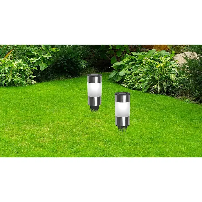 Globo Solarleuchten-Set Mini Tube - 0,06 W, Klar, Silber, IP44 - Zwei silberfarbene Solarleuchten stehen auf einem grünen Rasen, umgeben von Pflanzen. Die Leuchten sind ein Blickfang im Garten.