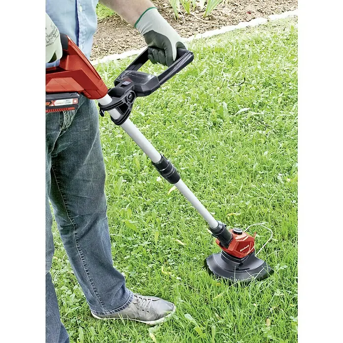 Einhell PXC 18V Recortabordes de batería GE-CT 18 Li-Solo - 18 V, Iones de litio, Sin batería - Una persona usa un cortabordes inalámbrico rojo Einhell en el jardín para cortar el césped. El cortabordes cuenta con un mango.