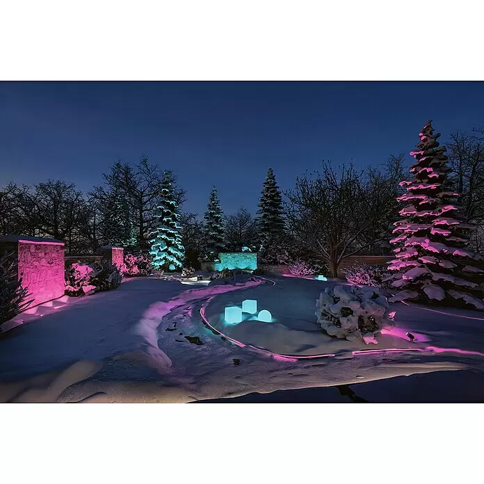 Paulmann Plug & Shine Erdspieß-Strahler Pike - 4,5 W, Höhe: 22,5 cm, IP44 - Ein verschneiter Wintergarten bei Nacht, beleuchtet von lebhaften pinken und blauen Lichtern, die Bäume, Steinmauern, leuchtende Würfel und einen Weg hervorheben.