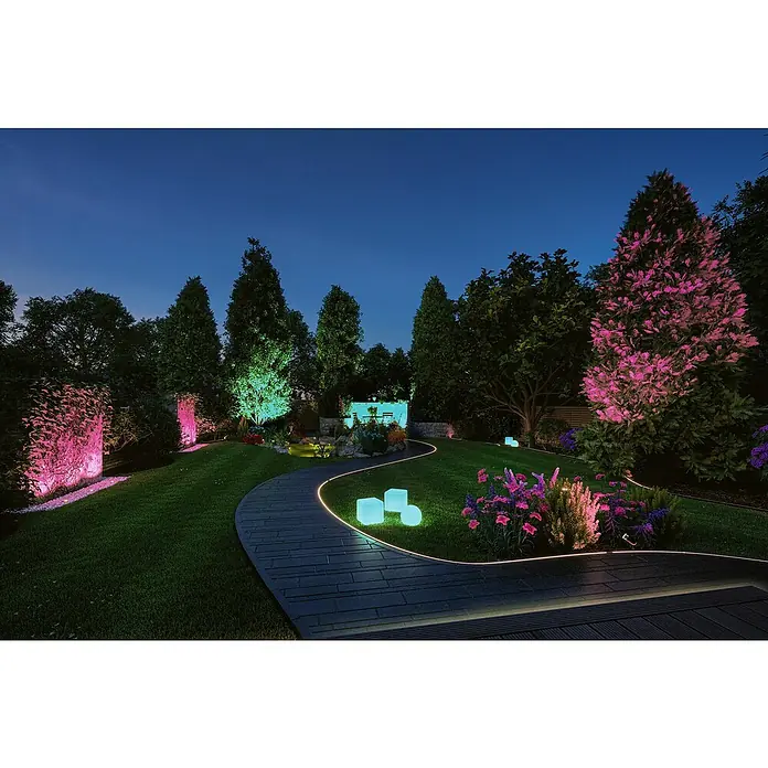 Paulmann Plug & Shine Basis-Set LED-Bodeneinbauleuchte Smart Home Zigbee - 3,6 W, Silber, Ø x H: 9,8 x 9,2 cm, Per App steuerbar, IP65 - Eine malerische Gartenlandschaft bei Nacht, illuminiert durch farbige Akzentbeleuchtung, die Bäume und Wege hervorhebt und eine magische Atmosphäre schafft.