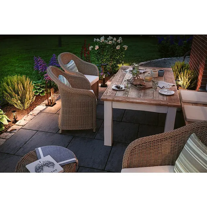 Paulmann Plug & Shine LED-Gartenstrahler Minipoller - Ø x H: 8 x 22 cm, 2 W, Anthrazit, IP44 - Eine malerische Gartenszene mit einem einladenden Esstisch und Korbstühlen, die von sanfter Beleuchtung akzentuiert werden.