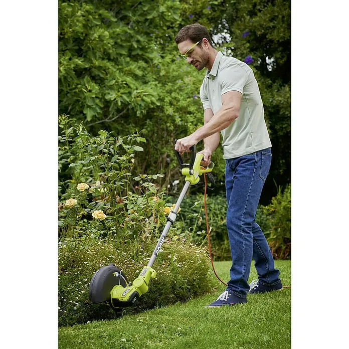 Ryobi Elektro-Rasentrimmer RLT6130 - 600 W, Schnittbreite Faden: 30 cm - Mann trimmt Rasen mit RYOBI Rasentrimmer. Der Trimmer ist grün und hat einen orangefarbenen Kabel. Er trägt eine grüne Schutzbrille.