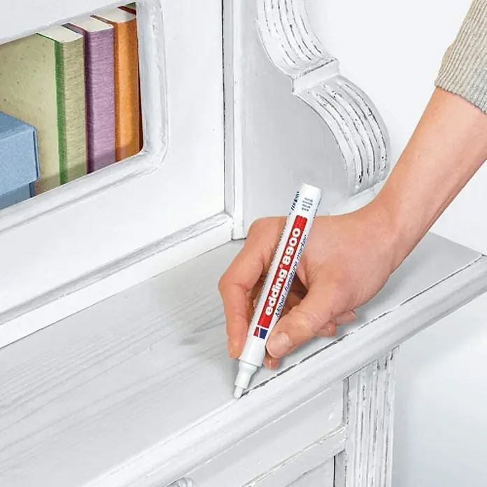 Edding Marcador permanente para muebles - Grosor de trazo: 1,5 mm - 2 mm, Blanco - Un rotulador para muebles Edding 8900 en acción, reparando arañazos y daños en una superficie de madera blanca. Ideal para reparaciones de muebles.