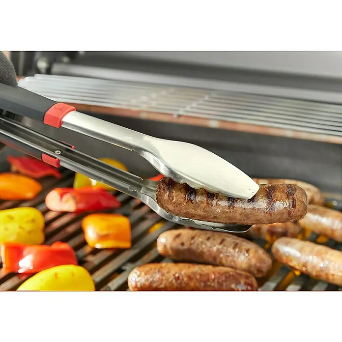 Weber Grillzange - Länge: 40,6 cm - Würstchen auf einem Grill, mit einer Grillzange in der Hand, umgeben von Paprika, die ebenfalls gegrillt werden.