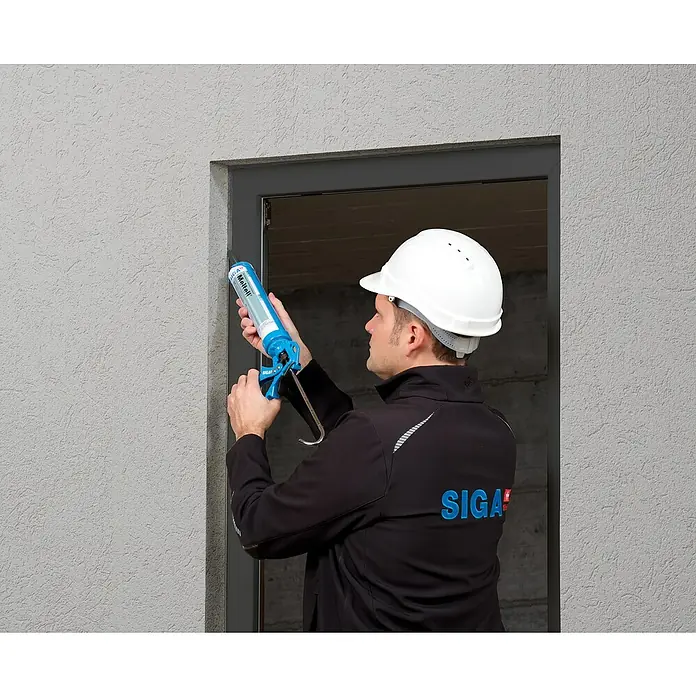 Siga Dichtmasse Meltell - 310 ml, Anthrazit - Mann mit SIGA-Jacke und Bauhelm verwendet eine Kartuschenpistole zum Abdichten eines Fensters.