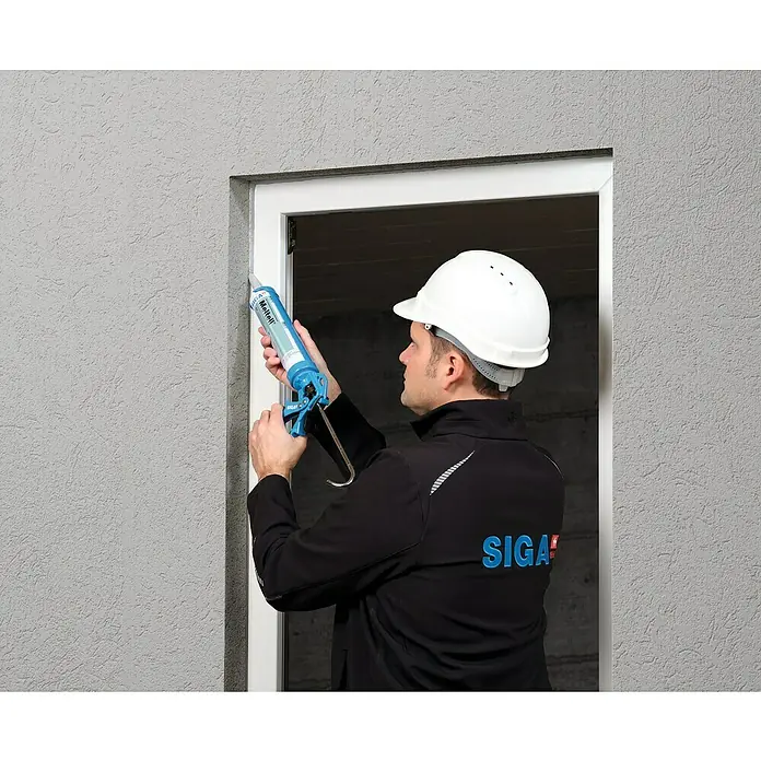 Siga Dichtmasse Meltell - 310 ml, Grau - Ein Mann mit Schutzhelm dichtet mit einer blauen Kartuschenpistole eine Fensteröffnung ab. Fokus liegt auf der Kartuschenpistole.