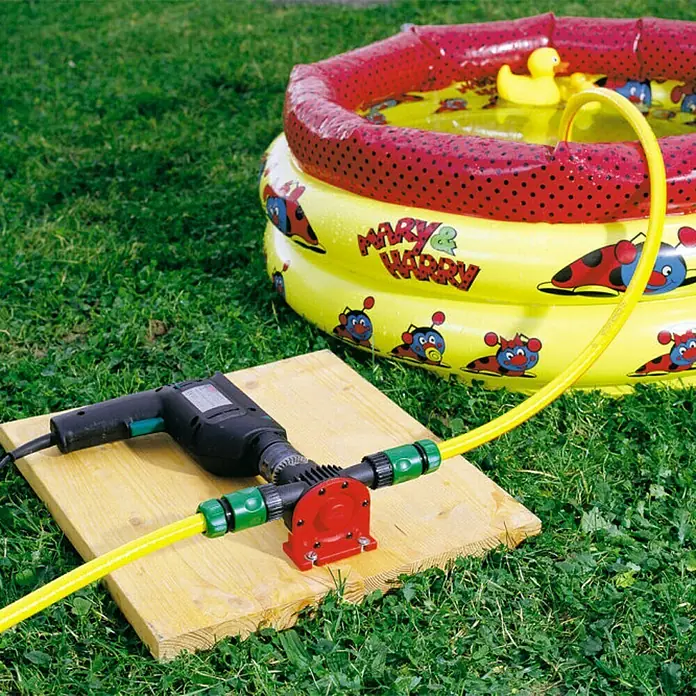 Wolfcraft Pumpe - 3.000 l/h, Förderhöhe: 19 m - 24 m, Kunststoff - Eine Bohrmaschine betreibt eine Pumpe auf einem Holzbrett, um ein aufblasbares Kinderbecken zu entleeren.