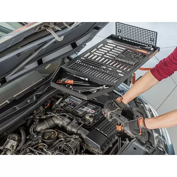 Bahco Materialständer Multi-Table BLEMAT1 - Höhenverstellung: 95 cm - 135 cm, Traglast: 50 kg - Schwarze Bahco Werkzeugablage, gefüllt mit verschiedenen Werkzeugen, über einem Automotor für einfachen Zugriff bei Reparaturen.