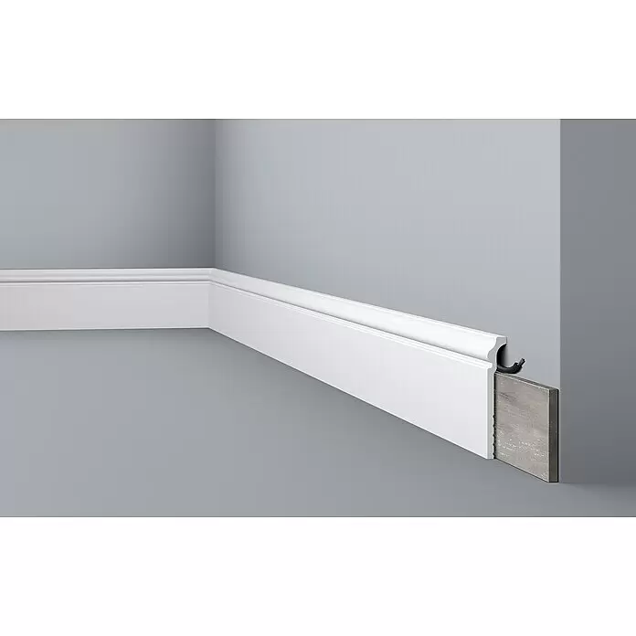 Nmc Decoflair Fußleiste Abdeckfußleiste CBC3 - 2 m x 2,2 cm x 12 cm, Hochverdichtetes extrudiertes Polymer (HDPS), 1 Stk. - Weiße Sockelleiste mit integriertem Kabelkanal, in einer Ecke installiert. Ein Querschnitt zeigt ein elektrisches Kabel und die Kante eines Holzbodens.