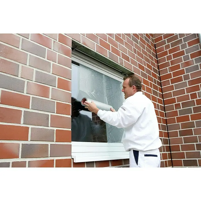 Kip Schutzfolie 213 - 100 m x 50 cm, Stärke: 0,05 mm - Ein Mann bringt eine Schutzfolie an einem Fenster an, um es vor Farbspritzern zu schützen. Die Folie ist auf einer Rolle aufgewickelt und wird angebracht.