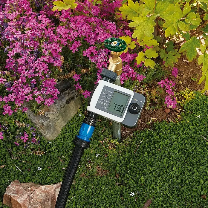 Programador de riego simple XD - ¾″, Específico para: 1 salida - Imagen de un temporizador de riego BHive conectado a un grifo, instalado en un entorno de jardín verde.