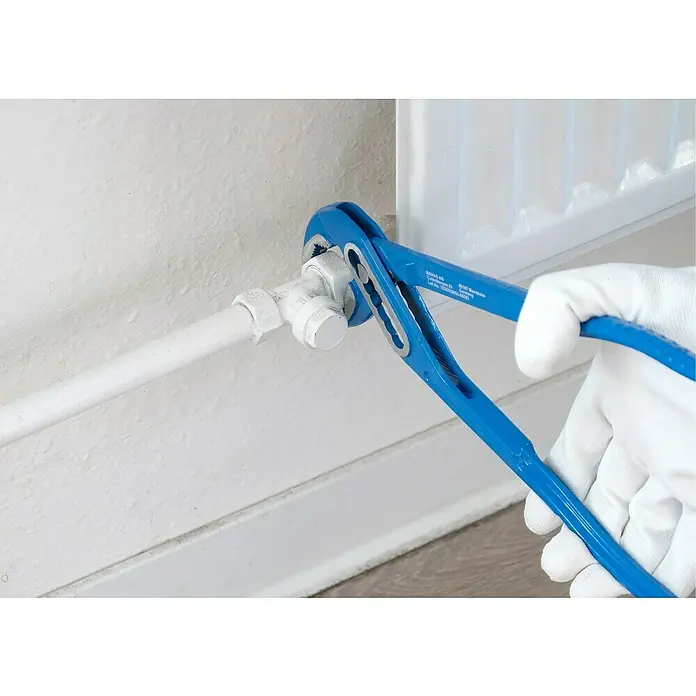 Alpha Tools Wasserpumpenzange - 3 -tlg. - Blaue Rohrzange wird verwendet, um ein weißes Rohr an einer Wand zu befestigen. Ein weiß behandschuhter Handgriff hält die Zange fest.