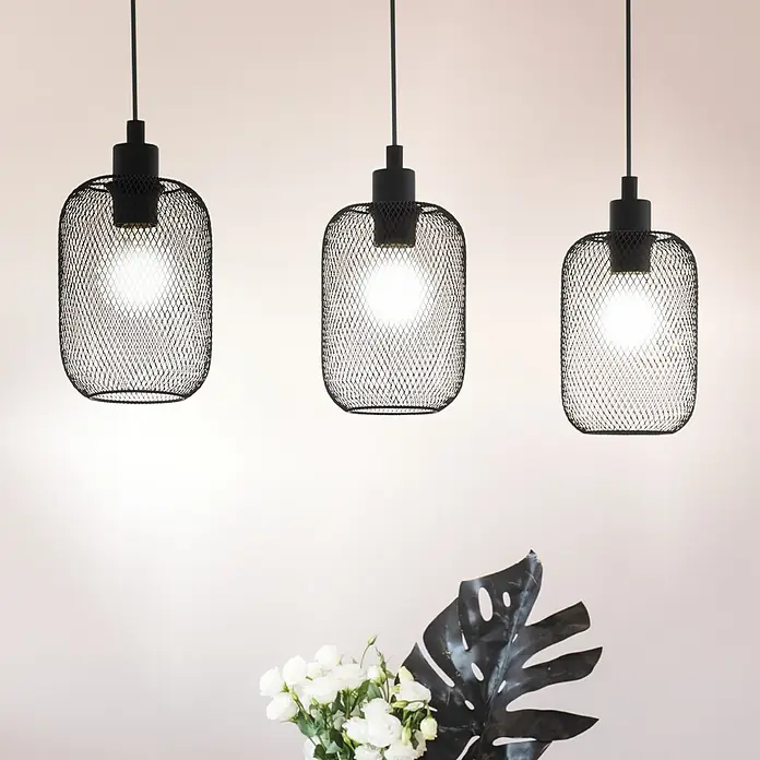 Eglo Wrington Pendelleuchte - 60 W, L x B x H: 74 x 15 x 11 cm, Schwarz, E27 - Das Bild zeigt drei moderne Hängelampen mit schwarzen, netzartigen Lampenschirmen über einem Tisch mit Blumen und einem Blatt.