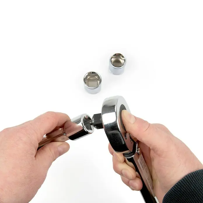Alpha Tools Drehmomentschlüssel - 28 Nm - 210 Nm, ½″, 5 -tlg. - Nahaufnahme einer Person, die eine Verlängerung an eine Chrom-Knarre befestigt, mit Stecknüssen im Hintergrund.
