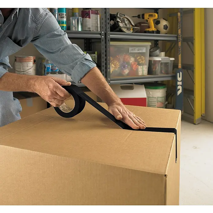 3M Cinta adhesiva universal Scotch americana - Negro, An x L: 48 mm x 25 m, 1 ud. - Una persona sujeta una caja de cartón con cinta aislante negra para asegurarla para el envío. La cinta se aplica con cuidado.