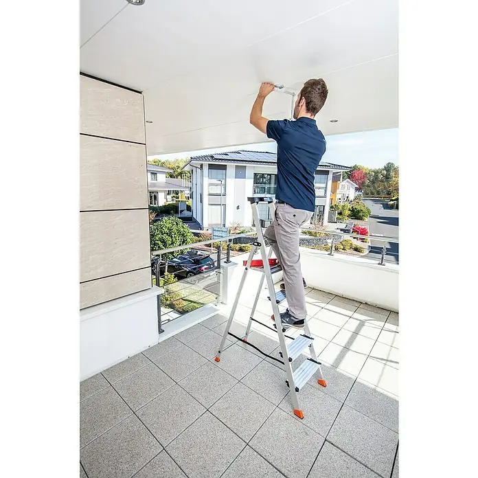 Krause Monto Stehleiter Sepuro - Anzahl Tritte: 5 Stk., Arbeitshöhe: 3,05 m, Aluminium - Ein Mann steht auf einer Klappleiter und befestigt eine Deckenleuchte. Die Leiter ist silberfarben und hat orangefarbene Füße.