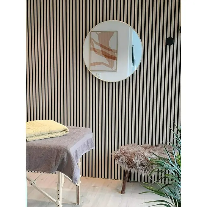 FibroTech Akustikpaneel Unika 25 - Light Oak, 2.440 x 600 x 22 mm - Wellness-Raum mit Massageliege, rundem Spiegel und flauschigem Hocker vor einer stilvollen Holzpaneelwand.