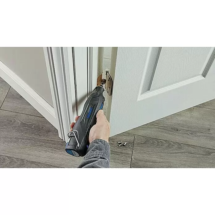 Dremel Akku-Rotationswerkzeug 8260-5 - 12 V, 1 Akku, 3 Ah, Leerlaufdrehzahl: 5.000 U/min - 30.000 U/min - Eine Hand hält ein schwarz-blaues Dremel Rotationswerkzeug und fräst damit eine Aussparung für ein Türscharnier in einem weißen Türrahmen.
