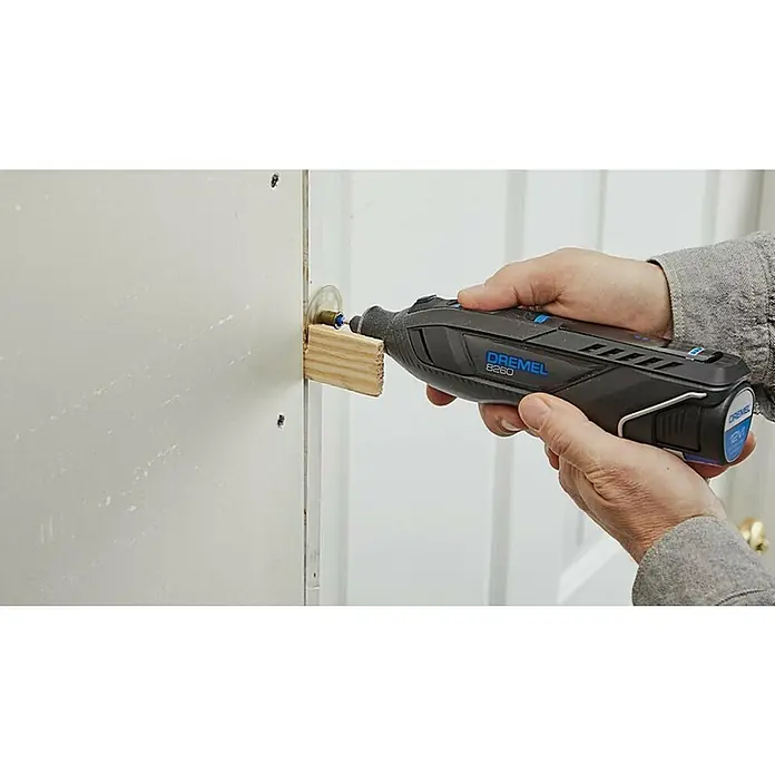 Dremel Akku-Rotationswerkzeug 8260-5 - 12 V, 1 Akku, 3 Ah, Leerlaufdrehzahl: 5.000 U/min - 30.000 U/min - Ein Dremel 8260 wird verwendet, um ein Loch in eine Tür zu schneiden. Der Dremel wird von einer Person gehalten und ist mit einem Aufsatz versehen.