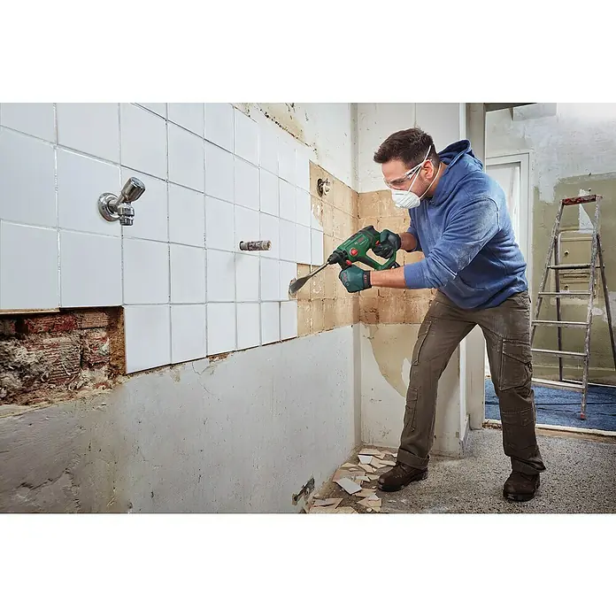 Bosch Power for All 18V Akku-Kombihammer UniversalHammer 18V - 18 V, Ohne Akku, 2 J - Ein Handwerker entfernt Fliesen mit einem Bosch-Bohrhammer in einem Badezimmer, Schutzbrille und Maske inklusive.