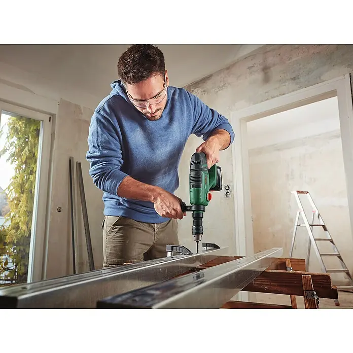Bosch Power for All 18V Akku-Kombihammer UniversalHammer 18V - 18 V, Ohne Akku, 2 J - Ein Mann bohrt mit einer Bosch-Bohrmaschine Löcher in Metallprofile, um ein Projekt im Haus zu realisieren. Er trägt eine Schutzbrille für die Arbeit.