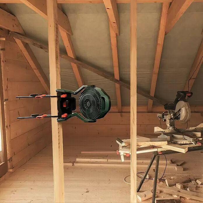Bosch Power for All 18V Akku-Ventilator UniversalFan 18V-1000 - 18 V, Ohne Akku, Luftmenge: 1.000 m³/h - Grün-schwarzer Ventilator an Holzbalken in ausgebautem Dachboden befestigt. Eine Gehrungssäge ist in der Nähe.