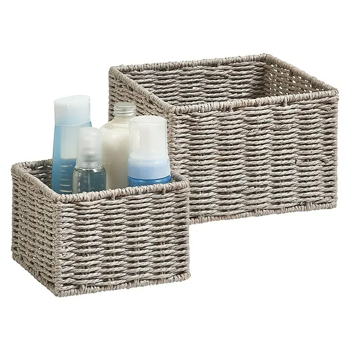 Zeller Present Juego de cestas Conjunto de 2 cestas para el baño - Gris, 2 pzs. - Dos cestas de almacenamiento de pasto marino tejido, una cesta más pequeña llena de artículos de baño y una cesta más grande vacía, contra un fondo negro.