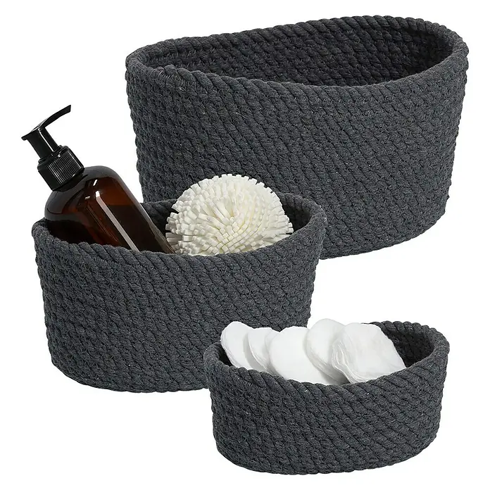 Zeller Present Juego de cestas trenzadas - Gris oscuro, 3 pzs. - Una disposición de tres cestas de mimbre de diferentes tamaños, llenas de accesorios de baño como loción, discos de algodón y una esponja de baño.