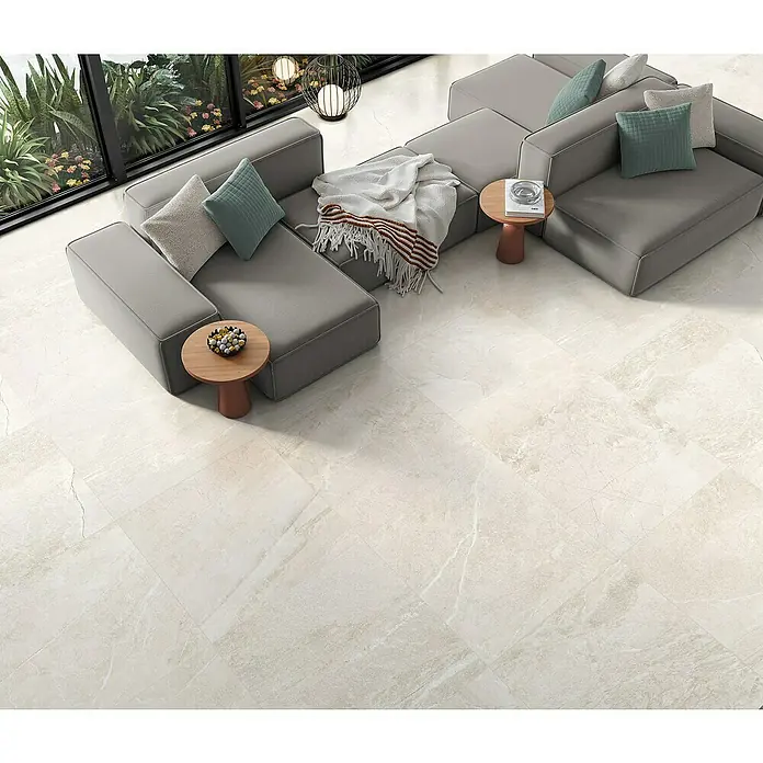 Halcón Pavimento porcelánico Tempo - 60 x 60 cm, Cotton, Mate, Rectificado - Vista de un salón moderno con sofás grises, mesas pequeñas y baldosas claras que crean un ambiente elegante y acogedor.