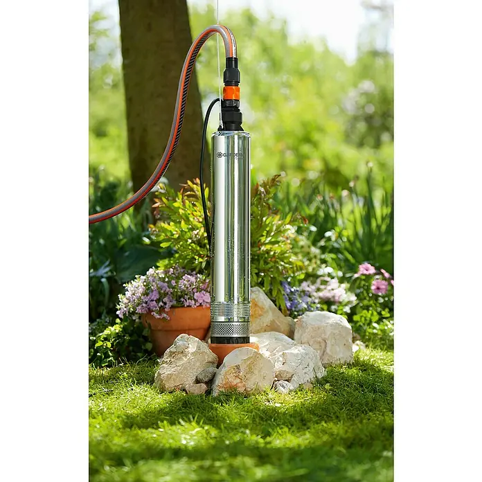 Gardena Tiefbrunnenpumpe 5500/5 Inox - 850 W, 5.500 l/h, Edelstahl - Die Gardena Tauchdruckpumpe 6000/5 automatic im Außenbereich, umgeben von Steinen und Pflanzen.