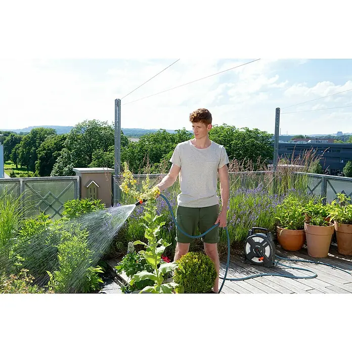 Gardena Schlauchtrommel - Schlauchlänge: 10 m, Kunststoff - Ein Mann bewässert Pflanzen auf einer Dachterrasse mit einem Gardena-Schlauch, dessen Trommel gut sichtbar ist.