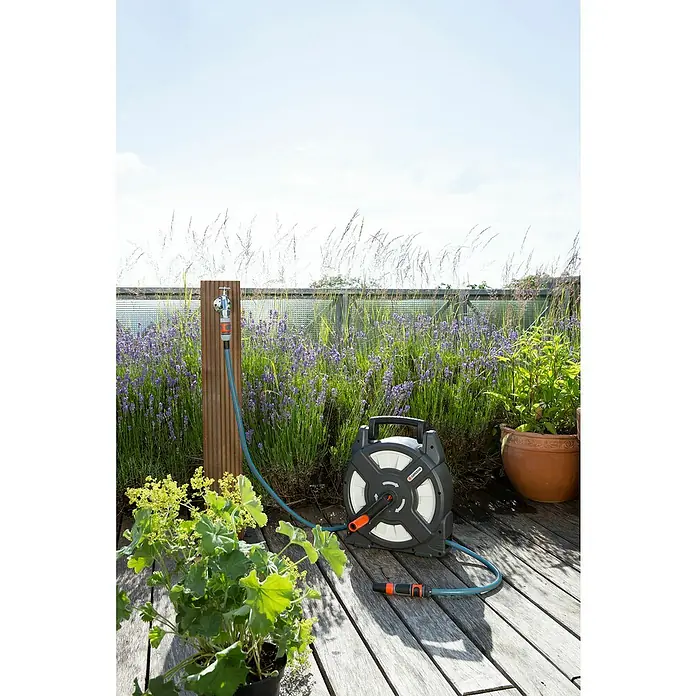 Gardena Schlauchtrommel - Schlauchlänge: 10 m, Kunststoff - Das Bild zeigt eine Gardena Schlauchtrommel auf einer Holzterrasse, eingebettet in blühende Lavendelbüsche und grüne Pflanzen.