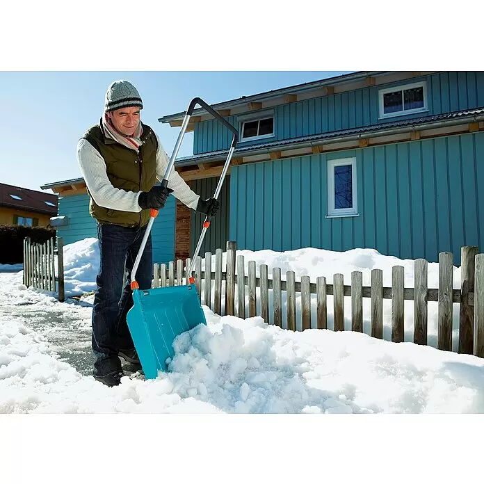 Gardena Schneewanne - Breite: 70 cm, Teleskopstiel, Kunststoff - Mann räumt mit einer blauen Kunststoff-Schneeschaufel und silbernen Griffen Schnee vor einem blauen Haus.