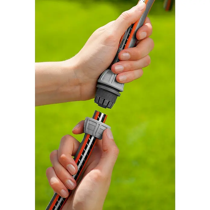 Gardena Reparator - 2 Stk. - Zwei Hände, die einen Gardena-Gartenschlauch mit orangefarbenen, weißen und schwarzen Streifen verbinden, wobei die grauen Anschlüsse im Fokus stehen.