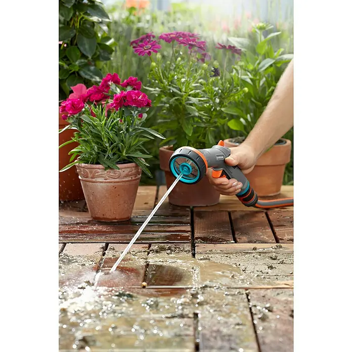 Gardena Comfort Vielflächenregner - Anzahl Sprühformen: 2 Stk., Kunststoff - Nahaufnahme einer Person, die einen Gartenschlauch mit Sprühkopf benutzt, um eine Holzterrasse zu reinigen.