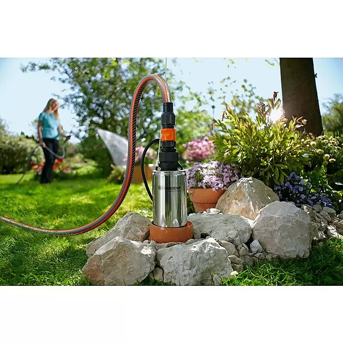 Gardena Tiefbrunnenpumpe 5500/5 Inox - 850 W, 5.500 l/h, Edelstahl - Gardena Tauchpumpe aus Edelstahl, mit grau-orangem Schlauch verbunden, zur Gartenbewässerung mit Person im Hintergrund.