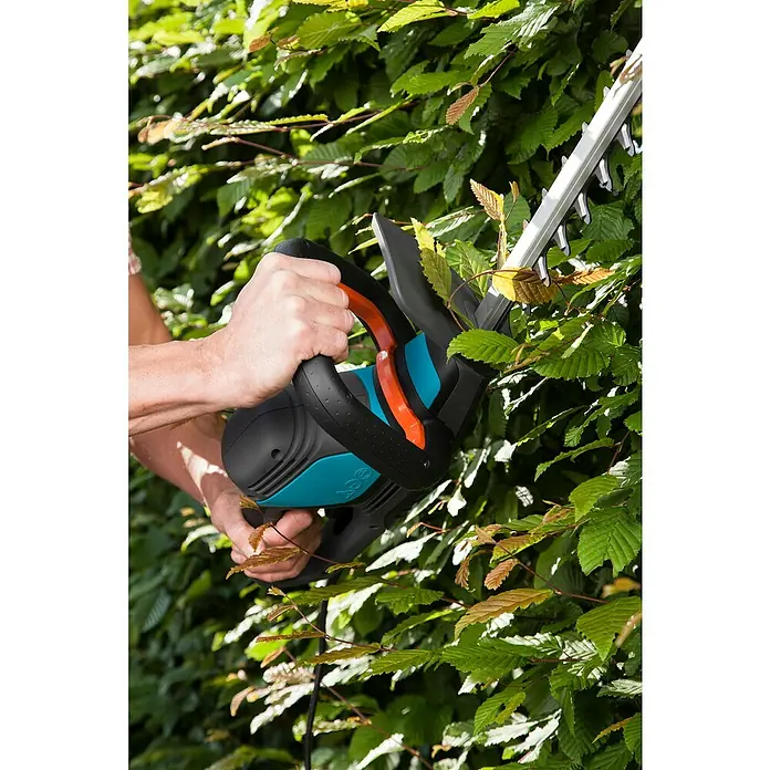 Gardena ComfortCut Elektro-Heckenschere 600/55 - 600 W, Schnittlänge: 55 cm - Eine Heckenschere von Gardena ist im Einsatz, um eine grüne Hecke zu schneiden. Die Schere hat blaue und schwarze Akzente.
