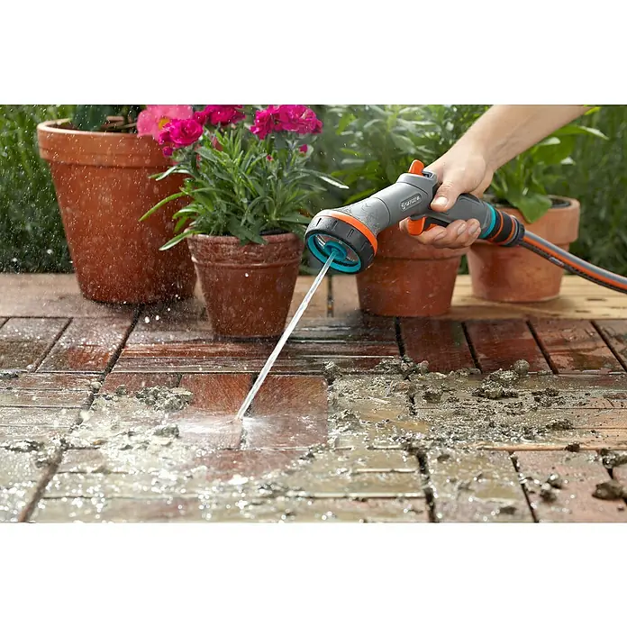 Gardena Comfort Vielflächenregner - Anzahl Sprühformen: 2 Stk., Kunststoff - Der verstellbare GARDENA Duschkopf wird zum Reinigen einer Terrasse im Freien mit einem Wasserstrahl verwendet. Blumen in Töpfen sind im Hintergrund.