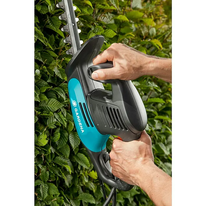 Gardena EasyCut Elektro-Heckenschere 450/50 - 450 W, Schnittlänge: 50 cm, Max. Aststärke: 18 mm - Eine Heckenschere von Gardena in Aktion, gehalten von zwei Händen, während sie eine Hecke schneidet.