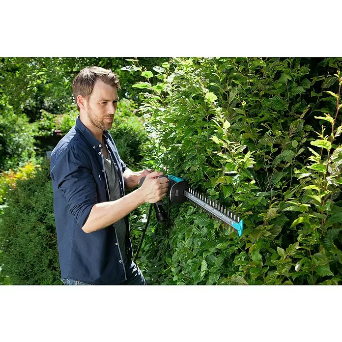 Gardena EasyCut Elektro-Heckenschere 500/55 - 500 W, Schnittlänge: 55 cm, Max. Aststärke: 18 mm - Ein Mann schneidet eine Hecke mit einer Gardena Heckenschere, wobei der Fokus auf dem Gartengerät und seiner Verwendung liegt.