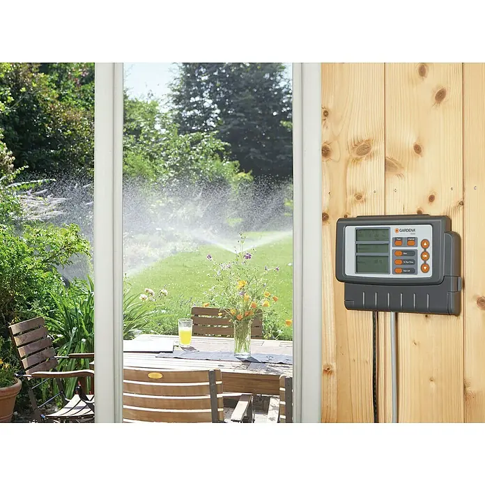 Gardena Classic Bewässerungscomputer 6030 - Bewässerungsdauer: 1 min - 3,59 h - Ein Gardena Bewässerungscomputer an einer Holzwand, der ein grünes Feld mit Bewässerung im Hintergrund steuert. Praktisch!