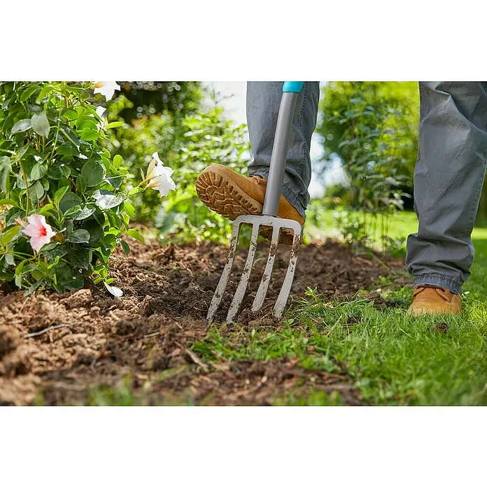 Gardena Ergoline Spatengabel - Anzahl Zinken: 4, Ergonomischer Stiel - Nahaufnahme einer Person, die mit einer Gartengabel den Boden umgräbt, ideal für Gartenarbeiten und Pflanzenpflege.